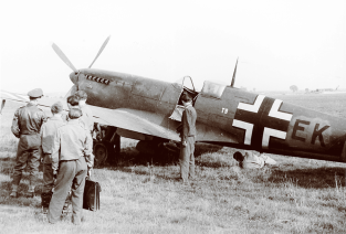 : Visiting Luftwaffe fighter pilots, possibly from JG 27, look over this captured Spitfire IX, which was an ex No. 412 (RCAF) Squadron machine that was lost in mid 1944. The aircraft carried the unit code T9+EK with enlarged national markings and a bright yellow tail unit to try and avoid wrong identification